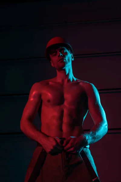 Sexy shirtless fireman in protective hardhat in darkness — Stock Photo