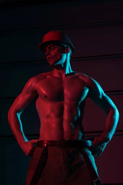 Sexy shirtless fireman in protective hardhat in darkness — Stock Photo