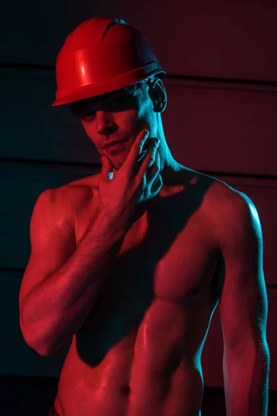 Sexy shirtless fireman in protective hardhat touching face and looking at camera in darkness — Stock Photo