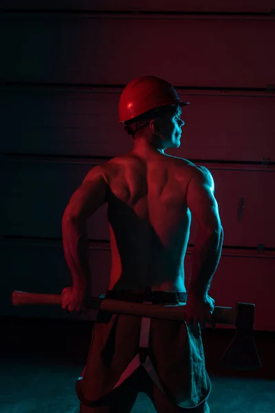 Back view of shirtless fireman holding flat head axe in darkness — Stock Photo