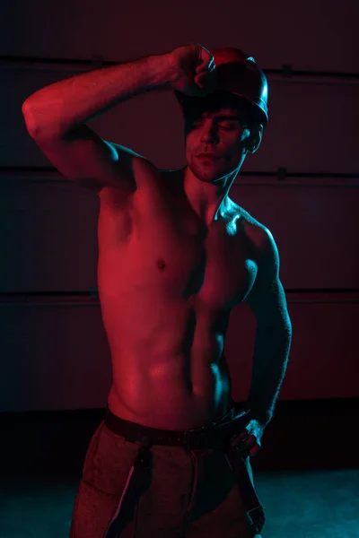 Sexy shirtless muscular fireman in protective helmet in darkness — Stock Photo