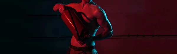 Panoramic shot of sexy shirtless fireman holding fire extinguisher in darkness — Stock Photo