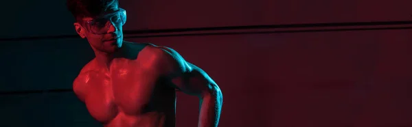 Panoramic shot of sexy shirtless fireman in protective goggles in darkness — Stock Photo