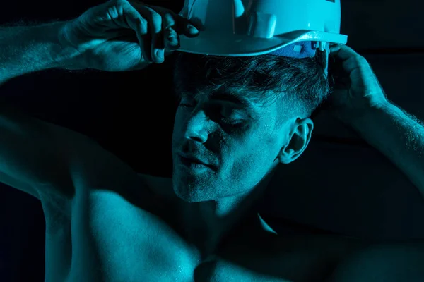 Sexy shirtless fireman touching protective hardhat in darkness — Stock Photo
