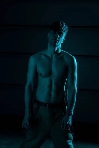 Sexy shirtless fireman in pants looking at camera in darkness — Stock Photo