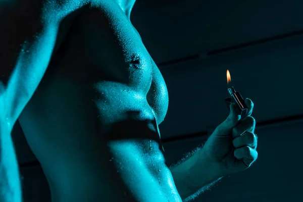 Обрезанный вид сексуального мужчины без рубашки, держащего светлее в темноте — стоковое фото