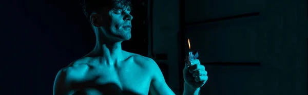 Panoramic shot of sexy shirtless man holding lighter with closed eyes in darkness — Stock Photo