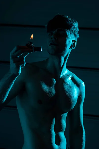 Sexy sem camisa muscular homem segurando mais leve na escuridão — Fotografia de Stock