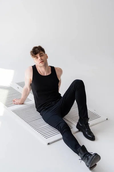Homme en chemise noire sans manches assis sur gris — Photo de stock