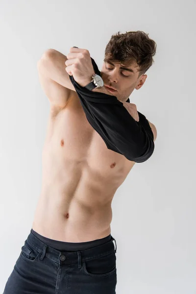 Сексуальный мускулистый мужчина снимает рубашку без рукавов изолированную на сером — Stock Photo