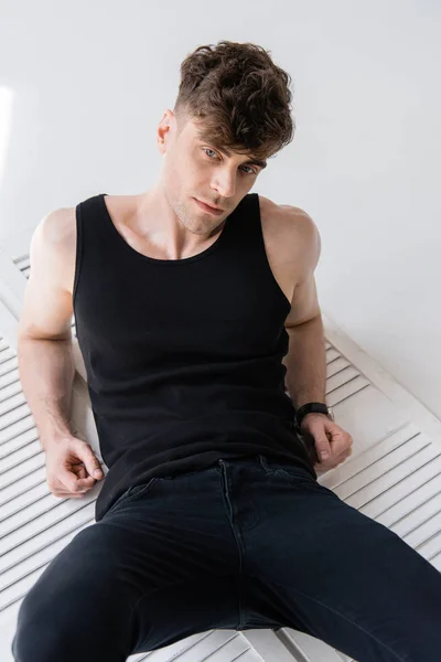 Pensive handsome man in black sleeveless shirt lying on grey — Stock Photo