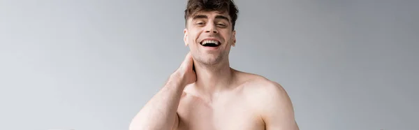 Panoramic shot of laughing shirtless man looking at camera isolated on grey — Stock Photo