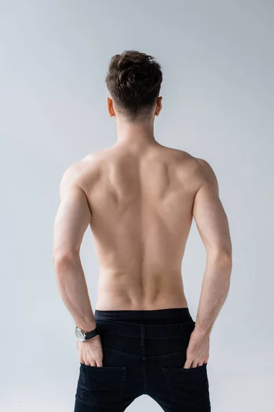 Vista posteriore di uomo muscoloso senza camicia in jeans con le mani in tasche isolate su grigio — Foto stock