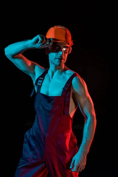 Sexy fireman in overall, hardhat and protective goggles isolated on black — Stock Photo