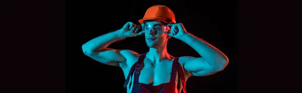 Colpo panoramico di sexy pompiere in generale, hardhat e occhiali protettivi isolati su nero — Foto stock