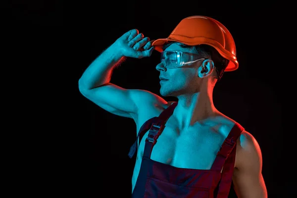 Sexy fireman in overall, hardhat and protective goggles isolated on black — Stock Photo