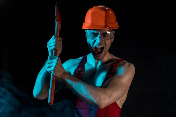 Worried shirtless fireman in hardhat and protective goggles holding flat head axe and screaming in smoke on black — Stock Photo