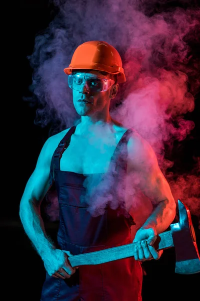 Serious shirtless fireman in hardhat and protective goggles holding flat head axe in smoke on black — Stock Photo