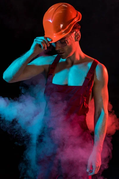 Sexy shirtless fireman in overall and hardhat in smoke on black — Stock Photo