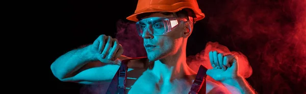 Panoramic shot of sexy shirtless fireman in overall and hardhat in smoke on black — Stock Photo