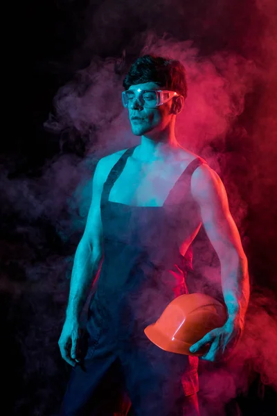 Sexy hemdlosen Feuerwehrmann in Overall hält Harthut in Rauch auf schwarz — Stockfoto