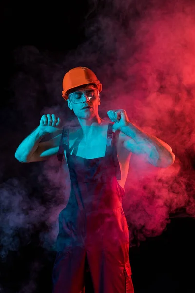 Sexy shirtless fireman in overall and hardhat in smoke on black — Stock Photo