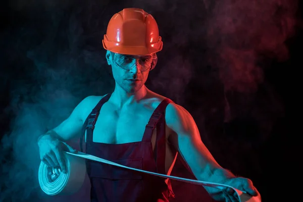Sexy pompier en hardhat et lunettes de protection tenant tuyau d'incendie en fumée sur noir — Photo de stock