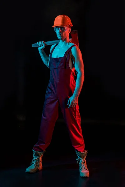 Full length view of sexy fireman in overall holding flat head axe on black — Stock Photo