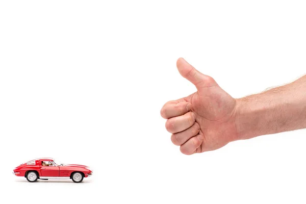 Vista recortada del hombre mostrando el pulgar hacia arriba y coche de juguete rojo en blanco - foto de stock