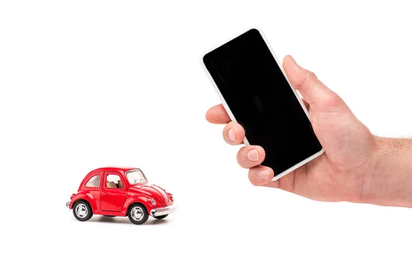 Обрезанный вид человека, держащего смартфон с пустым экраном и красной игрушечной машиной на белом — стоковое фото