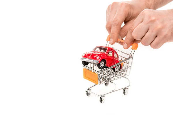 Vista recortada del hombre sosteniendo carro de la compra con coche de juguete rojo aislado en blanco - foto de stock