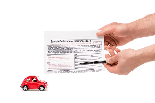 Vista cortada de homem segurando caneta e certificado de seguro perto de carro de brinquedo vermelho isolado no branco — Fotografia de Stock