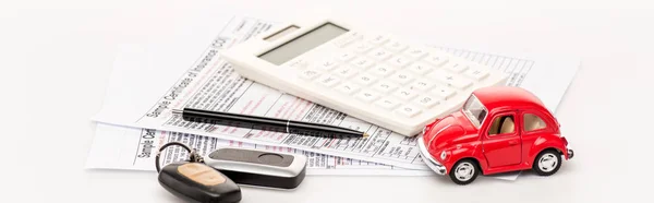 Panoramic shot of red toy car, keys, pen and documents on white surface — Stock Photo