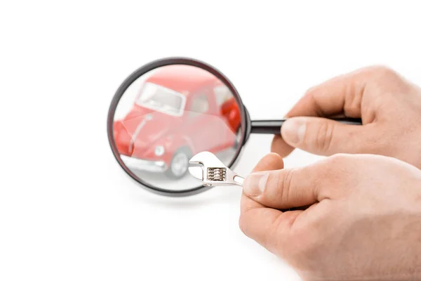 Cropped view of man holding magnifier and wrench in front of toy car isolated on white — Stock Photo