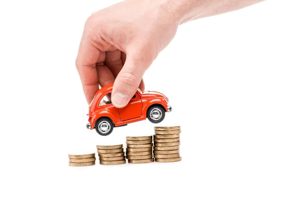 Vista cortada do homem segurando carro de brinquedo vermelho acima das moedas isoladas no branco — Fotografia de Stock