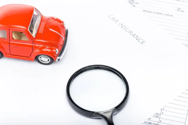 Red toy car, magnifying glass and insurance documents — Stock Photo