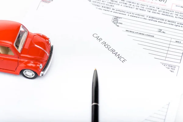 Auto giocattolo rossa, penna nera e documenti assicurativi — Foto stock