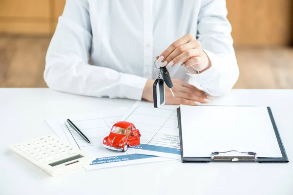 Vista recortada de la mujer en ropa formal con llaves en la mesa con documentos, coche de juguete, calculadora, pluma y portapapeles - foto de stock