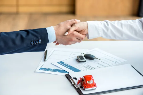 Ausgeschnittene Ansicht von Mann und Frau beim Händeschütteln am Tisch mit Dokumenten, Spielzeugauto, Schlüsseln und Klemmbrett — Stockfoto