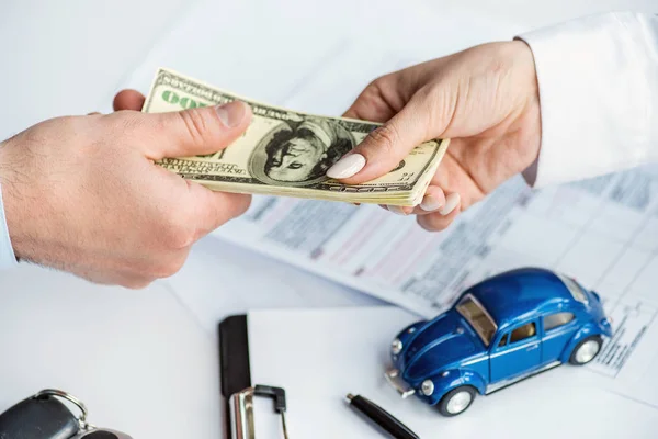 Vista recortada del hombre y la mujer sosteniendo billetes de dólar cerca de coche de juguete, portapapeles y documentos - foto de stock