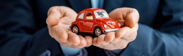 Colpo panoramico di uomo in abbigliamento formale che tiene auto giocattolo rosso — Foto stock