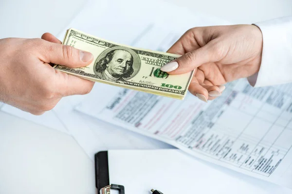 Vue recadrée de l'homme et de la femme tenant des billets en dollars près du presse-papiers et des documents — Stock Photo