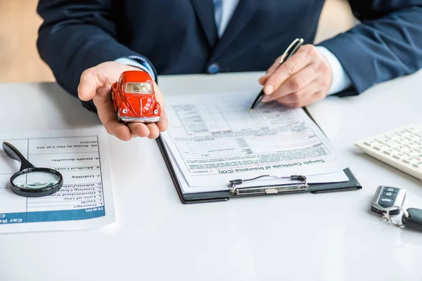 Vista parcial del hombre en desgaste formal sosteniendo coche de juguete rojo y documento de firma - foto de stock