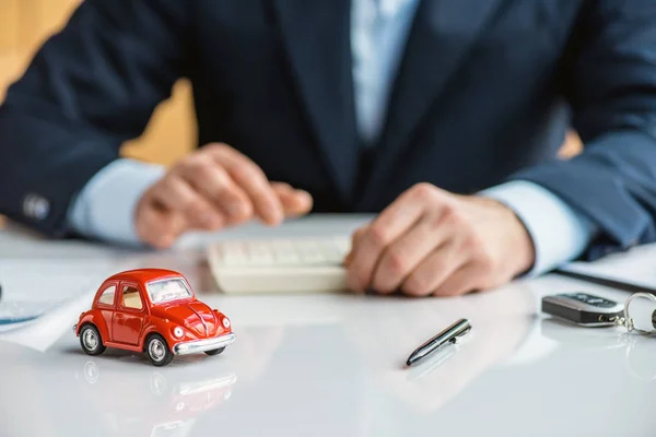 Foco seletivo do homem em desgaste formal à mesa com carro de brinquedo vermelho, caneta e chaves — Fotografia de Stock