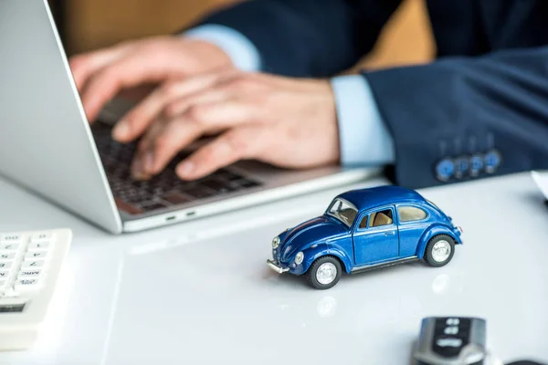 Enfoque selectivo del hombre en el desgaste formal usando el ordenador portátil en la mesa con el coche azul del juguete - foto de stock