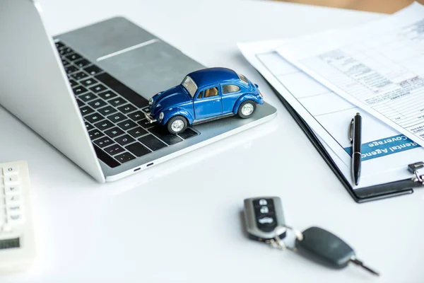 Ordinateur portable, voiture jouet bleu, presse-papiers, documents, clés et stylo sur la table — Photo de stock