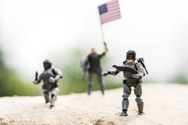 Selective focus of toy soldiers with weapon and american flag on sand — Stock Photo