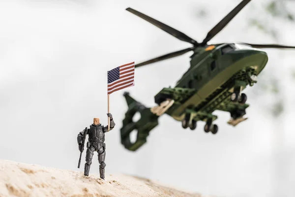 Игрушечный солдат с американским флагом, стоящий на песке возле вертолета — стоковое фото