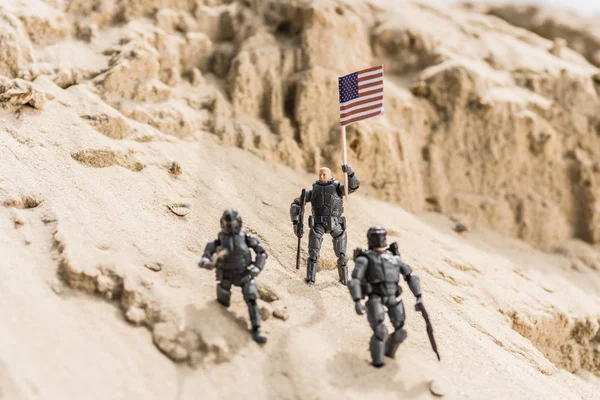Toy armed soldiers standing on sand and holding american flag — Stock Photo
