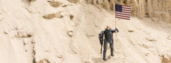 Spielzeug bewaffneter Soldat steht auf Sand und hält amerikanische Flagge in der Hand, Panoramaaufnahme — Stockfoto